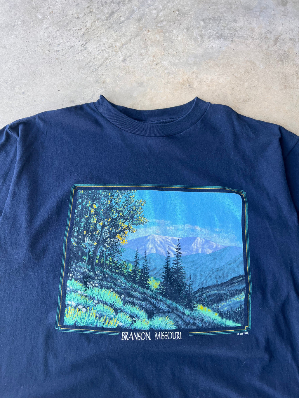 Blue t-shirt with a nature-themed graphic on a light gray surface